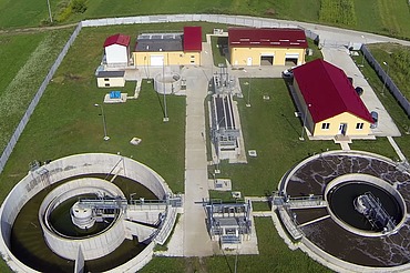 Luftaufnahme der Kläranlage von Moinești in Rumänien. Zu sehen sind runde Klärbecken, Behandlungsbecken, Kontrollgebäude mit roten Dächern und umliegende Grünflächen innerhalb eines eingezäunten Geländes.