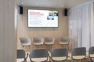 The presentation area fully prepared with a stage, empty seating, and the formal agenda for the upcoming expert talks displayed on a large screen.