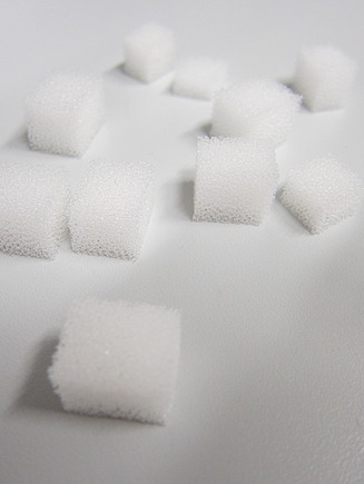 Mehrere kleine weiße LINPOR-Würfel aus porösem Material, die auf einer glatten Oberfläche angeordnet sind. Die Würfel haben eine schwammartige Beschaffenheit und sind gleichmäßig in gleichmäßige Formen geschnitten.