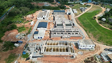 Luftaufnahme einer im Bau befindlichen großen Wasseraufbereitungsanlage mit mehreren Betonstrukturen, Tanks und einer umgebenden Grünanlage.