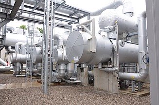 Große, isolierte Rohrbündelwärmetauscher und Hochleistungsrohrleitungen in einer Industrieanlage. Die silberverkleideten Einheiten sind Teil eines thermischen Verarbeitungssystems, das zur Energierückgewinnung oder Kühlung eingesetzt wird.