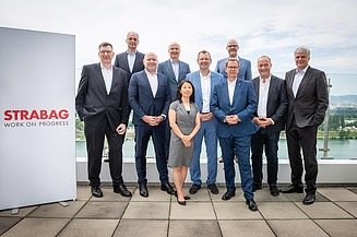 People standing together for a group photo on a terrace with a STRABAG display and an urban landscape behind them.