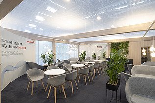 A dynamic perspective of the upper floor's glass facade featuring the STRABAG logo and hanging greenery.